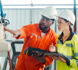 A man and a woman in hard hats and protective gear examine an advanced machine